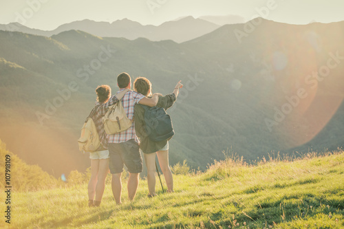 Three friends stand looking at panorama on mountain