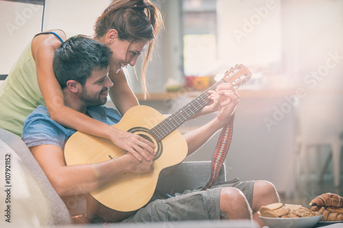 Young couple playing guitar on couch indoor