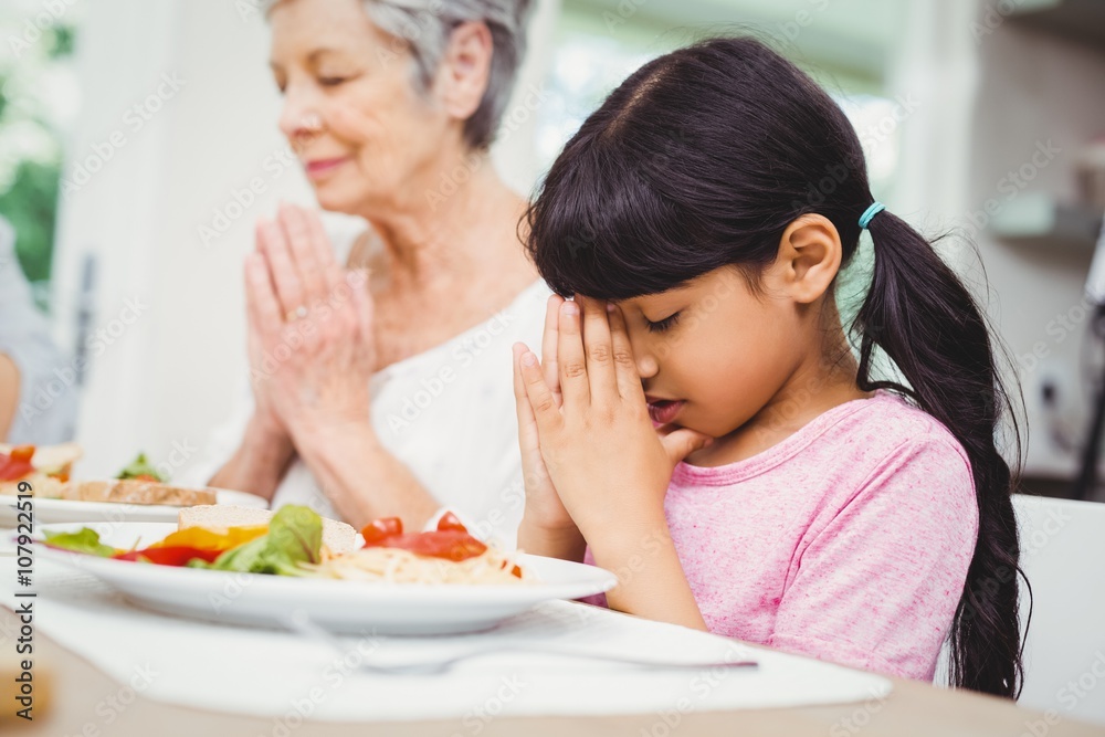 Granny and granddaughter praying at dining table Granny and granddaughter praying at dining table