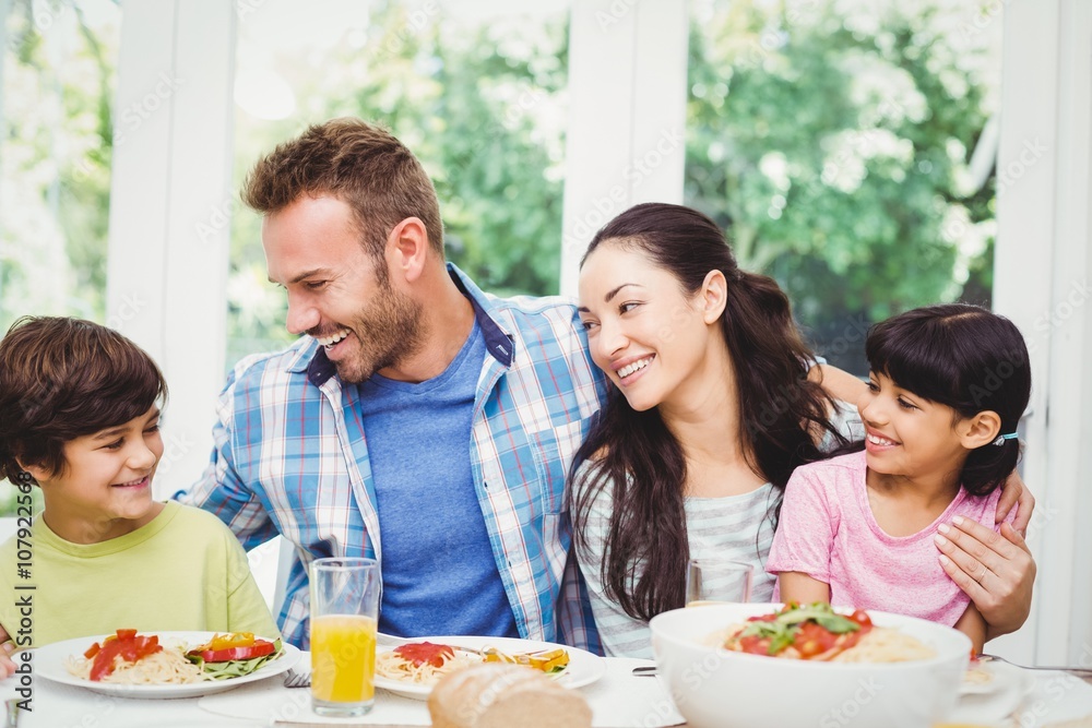 Smiling family with arm around while sitting at dining table Smiling family with arm around while sitting at dining table