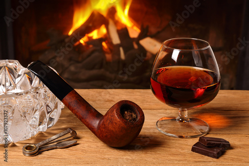 A glass of brandy, chocolate and tobacco pipe  on the background