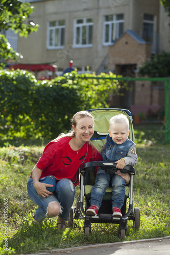 A little boy sitting in a wheelchair and walking with his mother