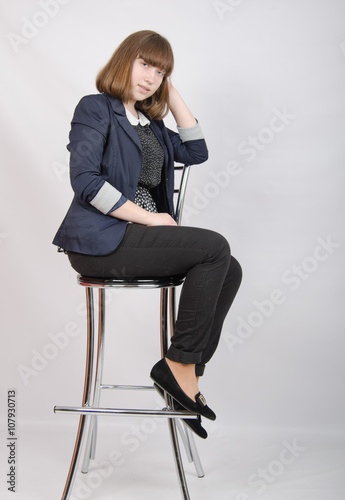 Девушка сидит на барном стуле на белом фоне
