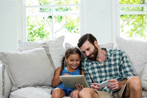Happy girl showing digital tablet to father on sofa