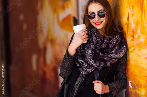 Pretty girl standing in front of wall with cup of coffee