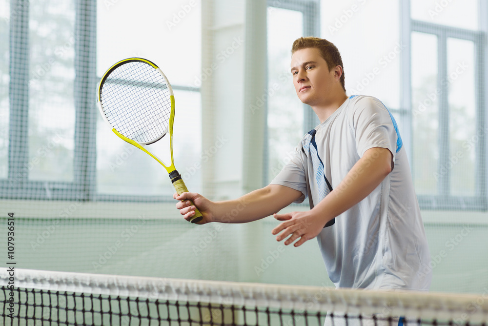 Low angle view of determined young man playing tennis indoor
