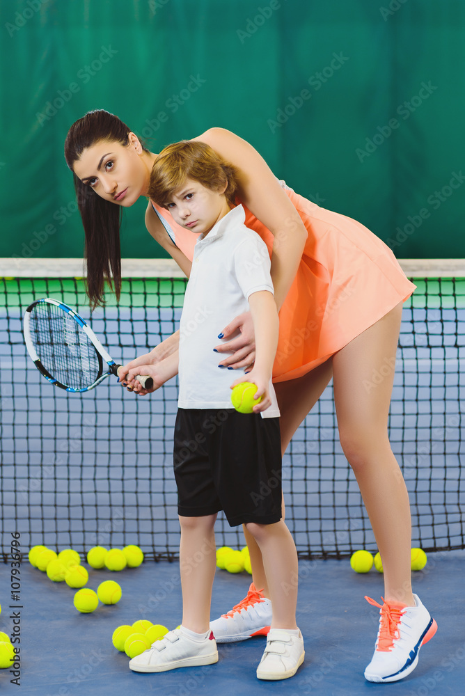 Young woman or coach teaching child how to play tennis on a court indoor