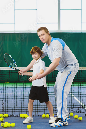 Instructor or coach teaching child how to play tennis on a court indoor