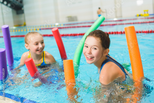 Happy and smiling group of children learning to swim with pool noodle