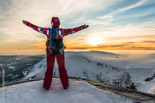 Young girl watching at the sunset on the top of mountains