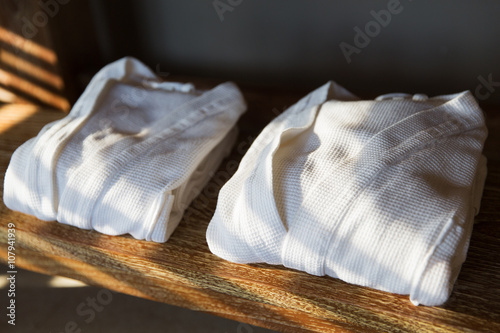 close up of two white bathrobes on wooden shelf photo