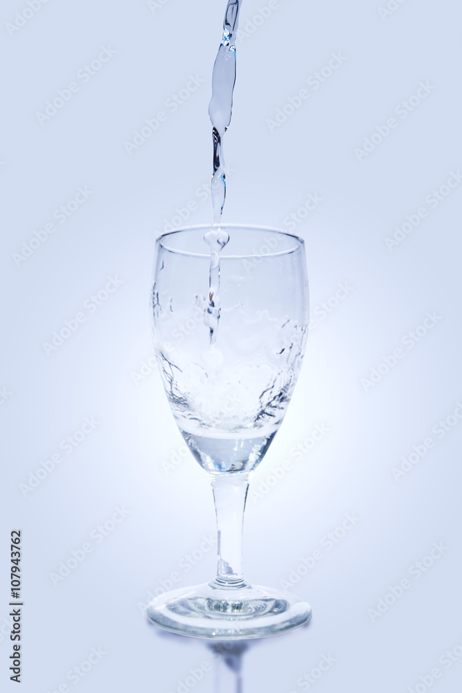 Pouring water into wine glass on blue background
