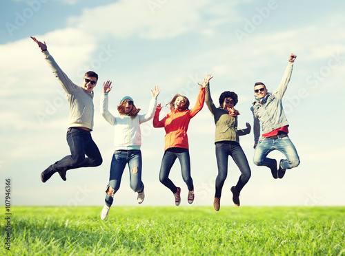 smiling friends in sunglasses jumping high