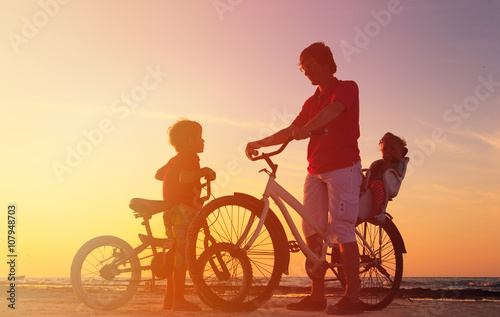 Biker family silhouette, father with two kids on bikes at sunset