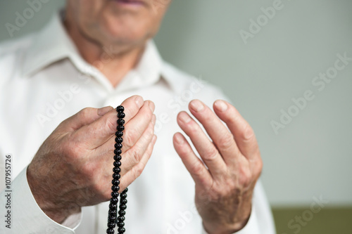 Praying hands of an old man holding rosary beads. Selective focus