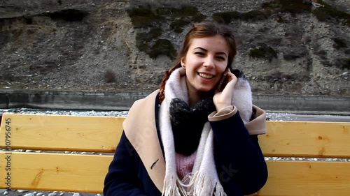 A young girl sitting on a bench outdoors and talking on the phone