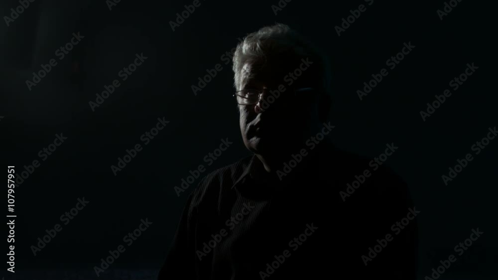 Middle-aged man with glasses sitting in a dark room and a lighter ignites the paper.
Middle-aged man with glasses sitting in a dark room and a lighter ignites the paper.