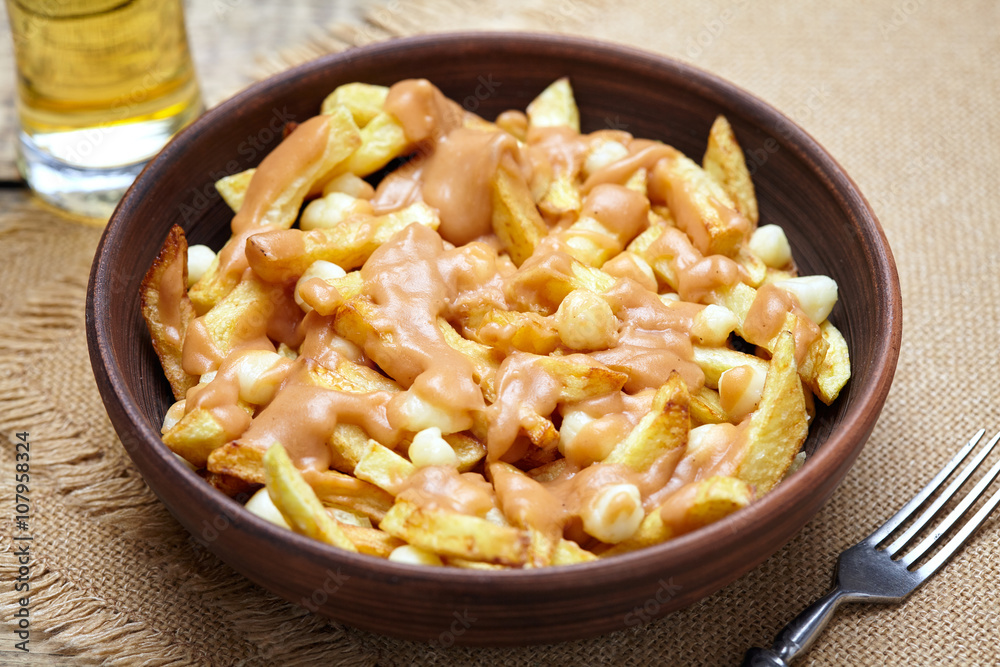 Poutine Canadian traditional fast food with fries, curd cheese and gravy on vintage wooden table background. Rustic style Poutine Canadian traditional fast food with fries, curd cheese and gravy on vintage wooden table background. Rustic style