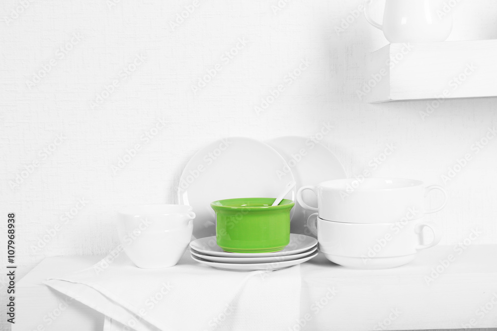 Set of tableware with napkin on shelf against white wall background Set of tableware with napkin on shelf against white wall background