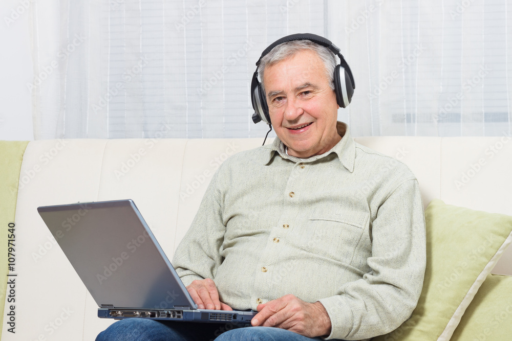 Senior man sitting on sofa with headphones and using laptop. Senior man sitting on sofa with headphones and using laptop.