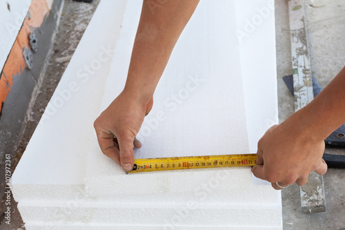 Thermal insulation house foundation walls with styrofoam boards. Worker use ruller to measure the correct length of styrofoam