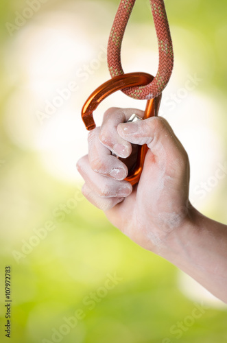 Man´s hand holding a carabine on a rope. Climbing equipment on a natural background. Hand in powder chalk magnesium. 