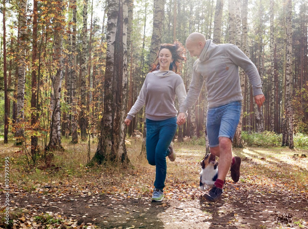 Fototapeta premium Couple running in the park with a Welsh Corgi Cardigan