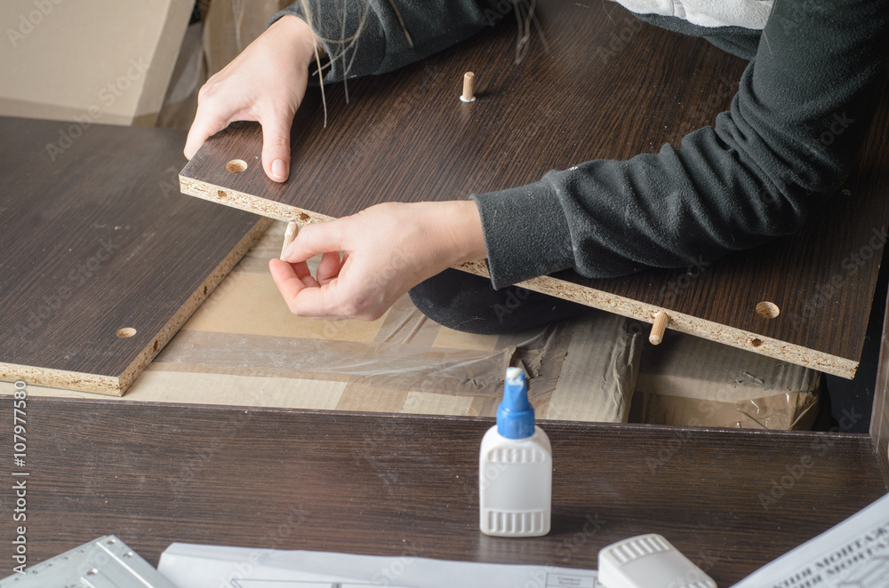 Man dressed in workers' overall assembling furniture sitting on the