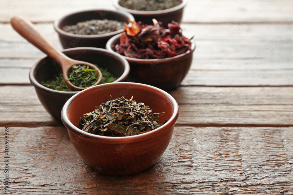 Variety of tea in round bowls with spoon on wooden table, close up Variety of tea in round bowls with spoon on wooden table, close up