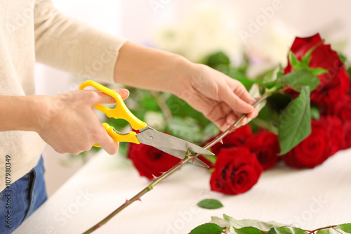 Woman cutting red rose from bouquet, indoors