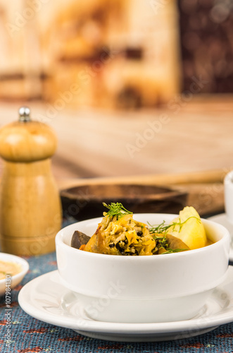 Classy serving of potato soup with meat and vegatables, served in white bowls sitting on table, blue tablecloth, salt pepper shakers, cozy restaurant background