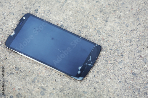 Broken mobile phone with cracked screen on the pavement