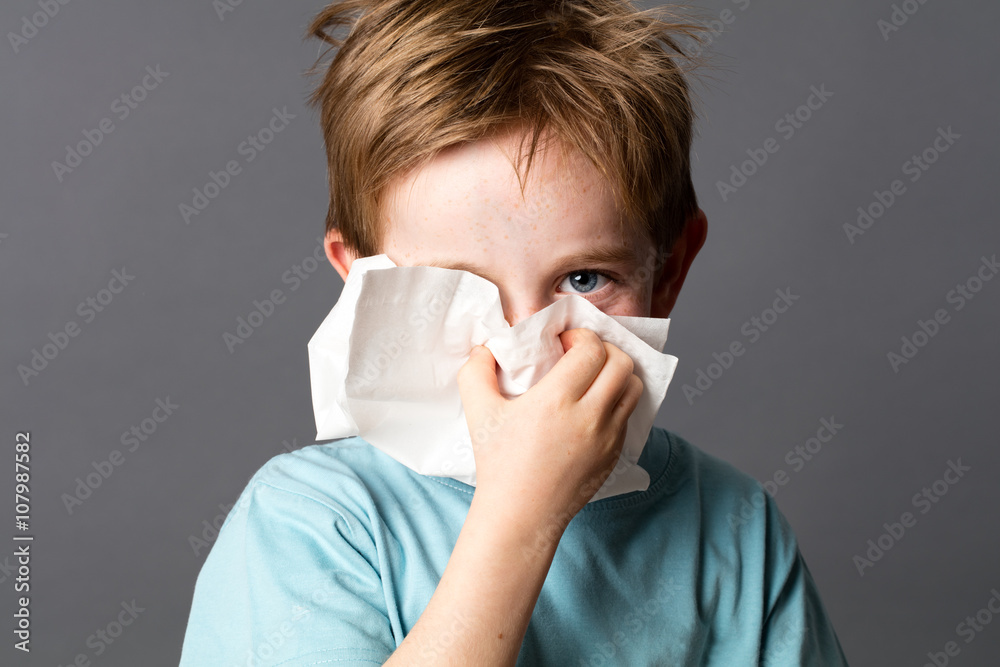 healthcare learning - cute little child with red hair and blue eyes hiding with a tissue to clean his nose from a cold or having hay fever, grey background studio healthcare learning - cute little child with red hair and blue eyes hiding with a tissue to clean his nose from a cold or having hay fever, grey background studio