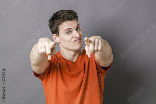 staring concept - happy handsome young sporty man provoking someone with his index fingers in the foreground, grey background