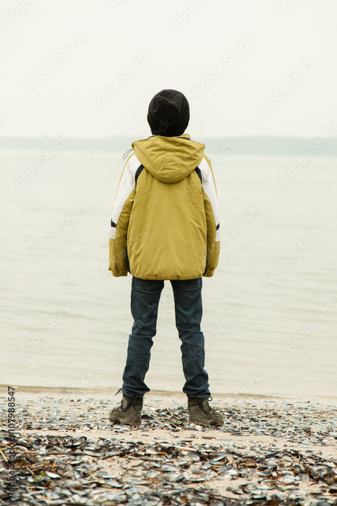 Single boy facing lake from shoreline