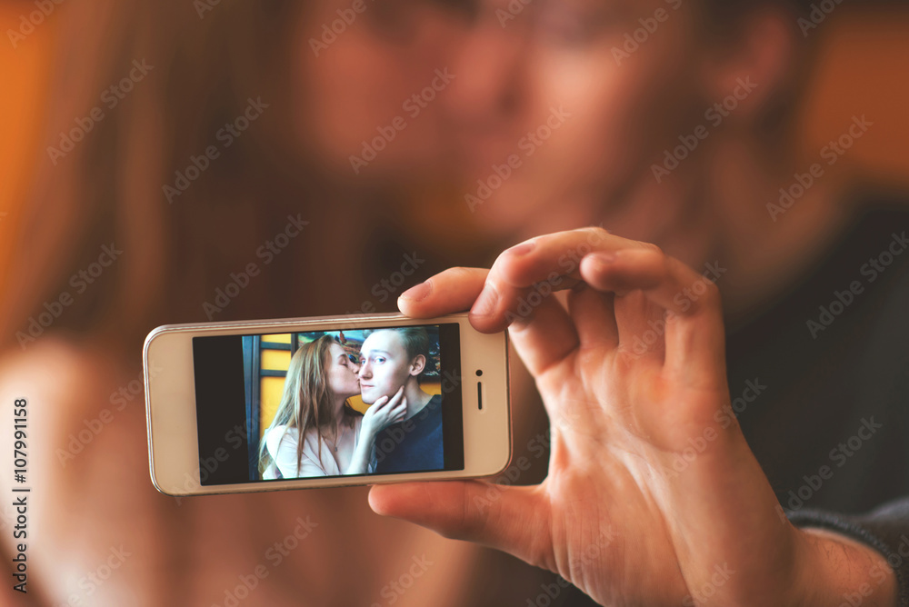 young couple kissing and photographing themselves on the phone