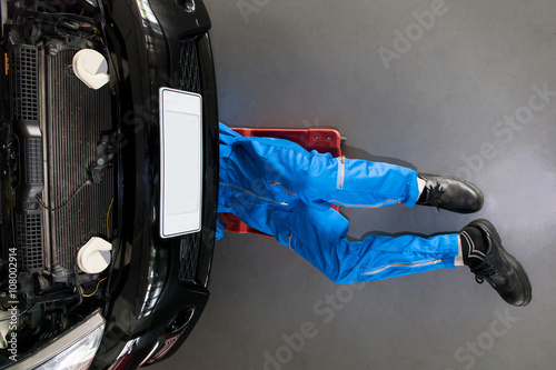 Bilde på lerret Mechanic in blue uniform lying down and working under car at the