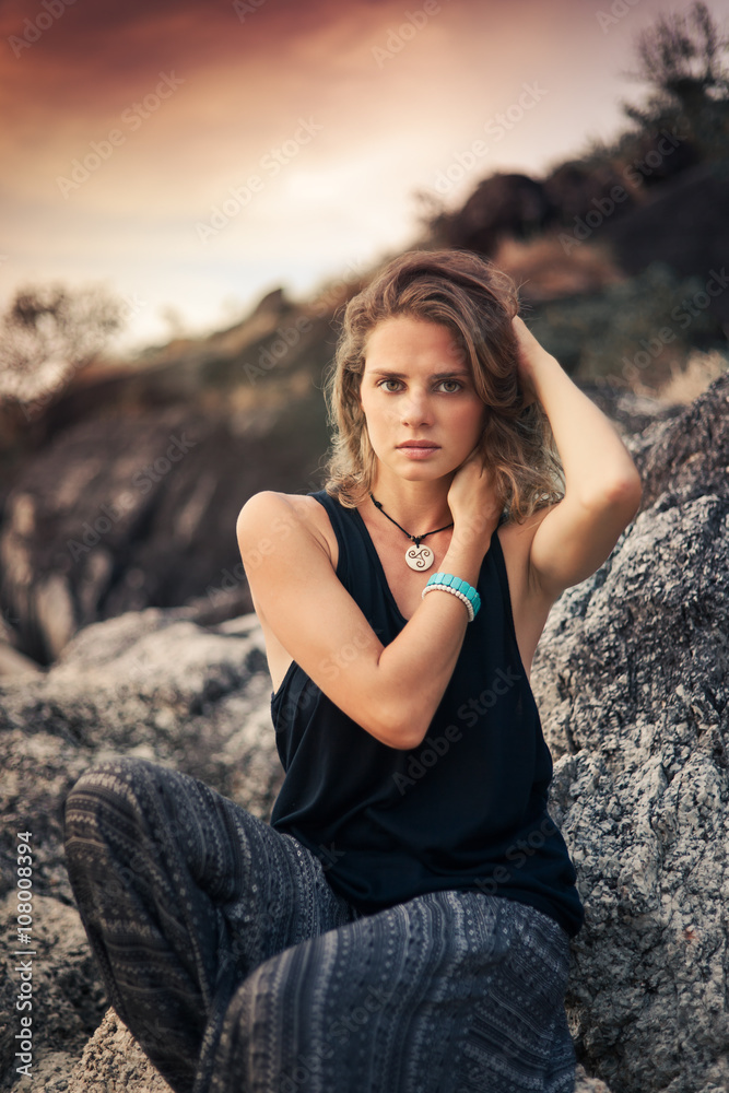 beautiful young woman sitting on the rocks at sunset background beautiful young woman sitting on the rocks at sunset background