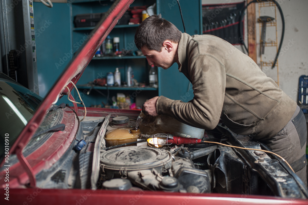 Mechanic man worker pouring antifreeze in the cooling system. Car repair works in auto service center Mechanic man worker pouring antifreeze in the cooling system. Car repair works in auto service center