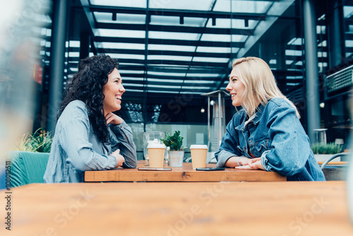 Tableau sur toile Two friends talking and drinking coffee, sitting in a cafe outdo