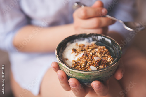 Young woman with muesli bowl. Girl eating breakfast cereals with nuts, pumpkin seeds, oats and yogurt in bowl. Girl holding homemade granola. Healthy snack or breakfst in the morning. photo