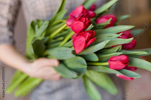 Fototapeta Naklejka Na Ścianę i Meble -  Young woman holding a beautiful bunch of red  tulips in her hands. Spring present for a girl in a grey dress. Flowers bouquet