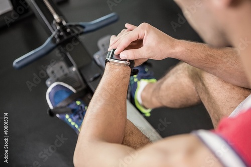 Muscular man on rowing machine using smart watch