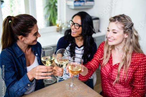 Cheerful female friends toasting wineglass at table in house