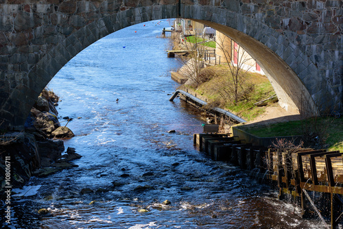 The Lyckeby river flows under a stone bridge. A fish ladder and part of the industrial properties on the other side of the bridge are seen. Freshwater leak out from the fishladder.