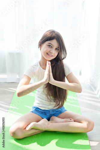 little girl doing gymnastics on a green mat for yoga. children's fitness, yoga for children. doing fitness exercise and stretching in a bright room. lotus Pose