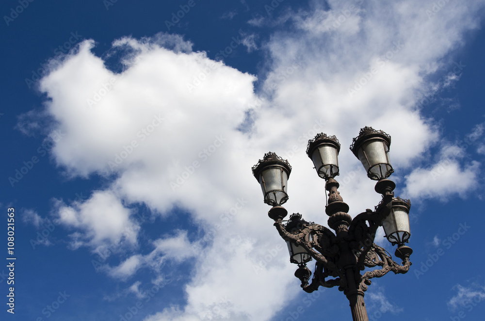 Old street lamps in front of a clear blue sky and white clouds