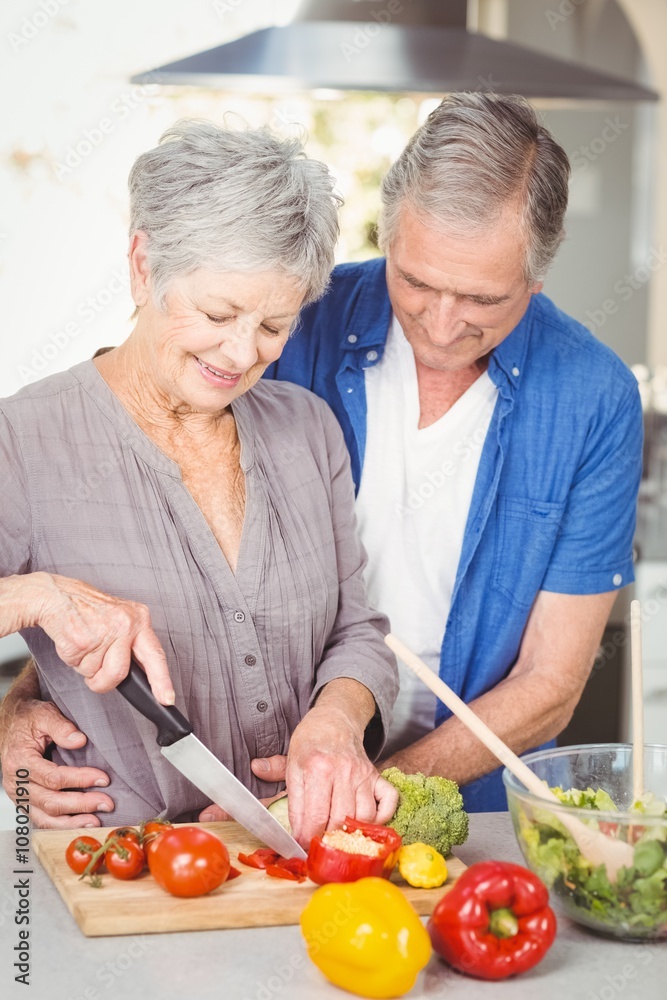 Senior woman cutting while man embracing in kitchen