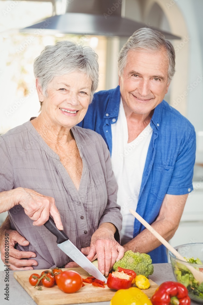 Portrait of senior woman cutting while man embracing in kitchen Portrait of senior woman cutting while man embracing in kitchen