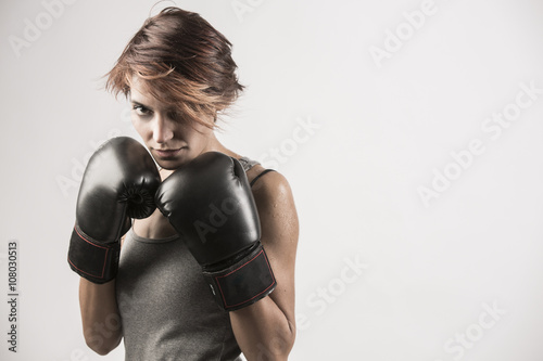 Donna Boxer sta in posizione di guardia con i guanti neri e la canotta grigia su fondo bianco © alex.pin